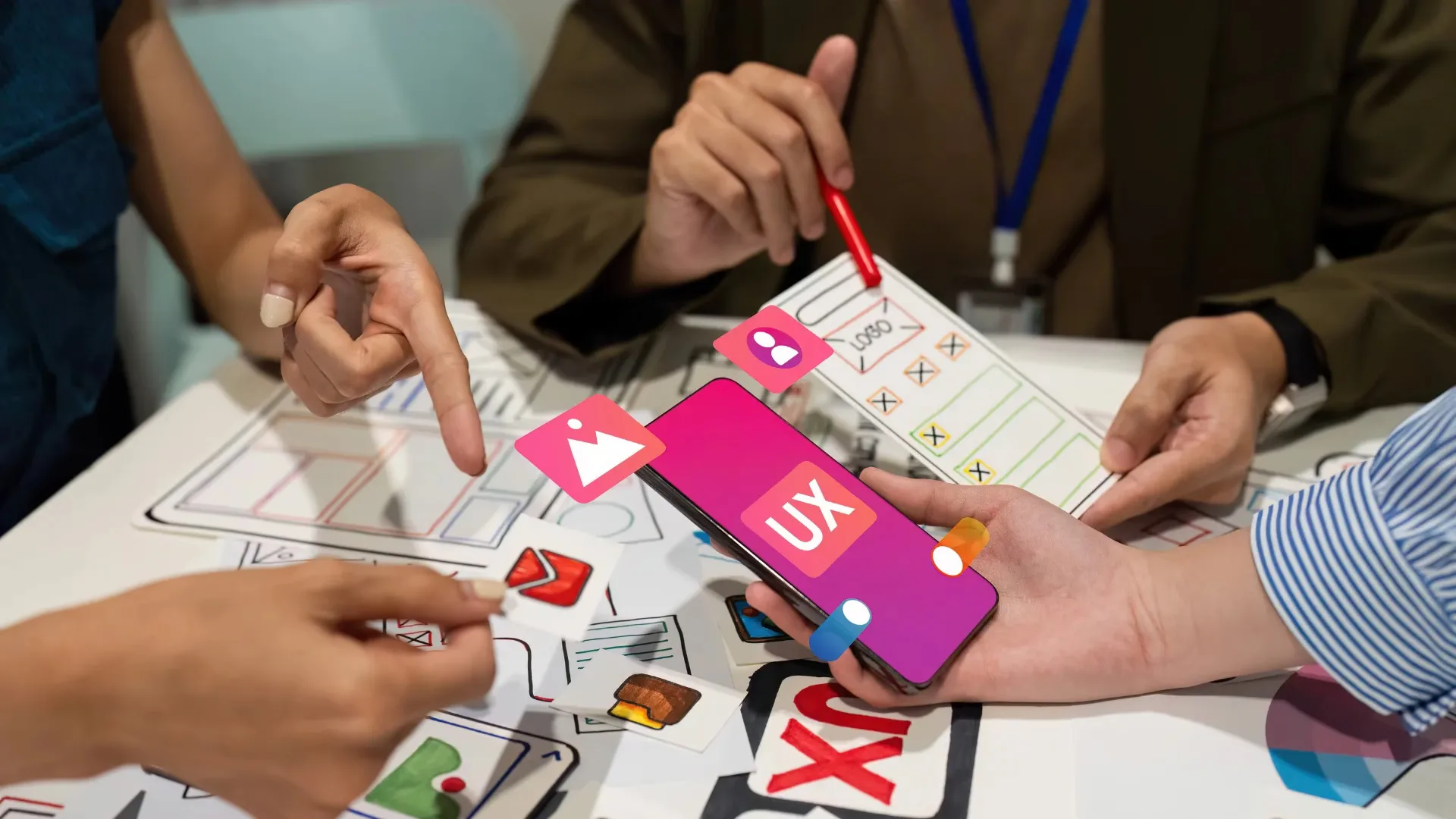 Team collaborating on mobile app and website UX design, with hands arranging sketches and a smartphone displaying a “UX” screen, illustrating the importance of mobile-first websites for Hyderabad businesses in 2025.
