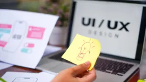 Designer working on UI/UX wireframes and website layout on a laptop and tablet, highlighting the role of UI/UX design in business website growth and user engagement.